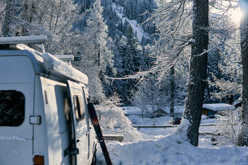 Snowy landscape with a camper van surrounded by frosted trees and mountains in winter