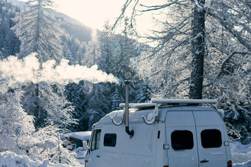 Obraz premium Winter scene with a white van releasing smoke in a snowy forest setting during daylight hours