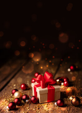 Abstract Christmas Background - Gift box with red bow and baubles on wood - Magic dark golden bokeh lights background - Ideal for Christmas greeting card on social media
