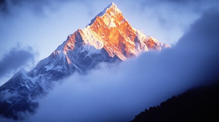 Majestic snow-capped mountain peak emerges through misty clouds, illuminated by a breathtaking sunrise.