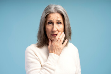 Portrait of shocked senior gray haired woman touching face looking at camera