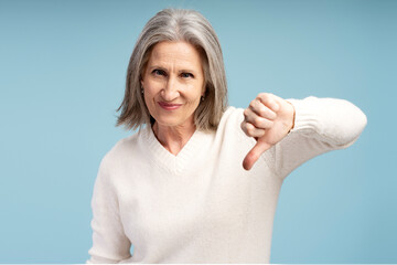 Fototapeta premium Portrait of serious senior woman showing dislike, looking at camera thumb down