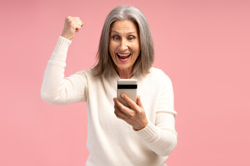 Portrait of happy, smiling, senior woman holding mobile phone, win money, hands up