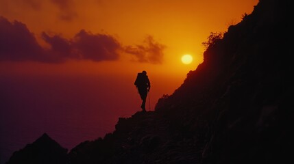 Obraz premium A silhouetted hiker climbs a rugged path against a dramatic sunset, embodying adventure and perseverance at the edge of an expansive, fiery horizon.