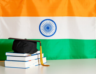 Graduation day of Indian university. Bachelor's hat on stack of books with Indian flag in...