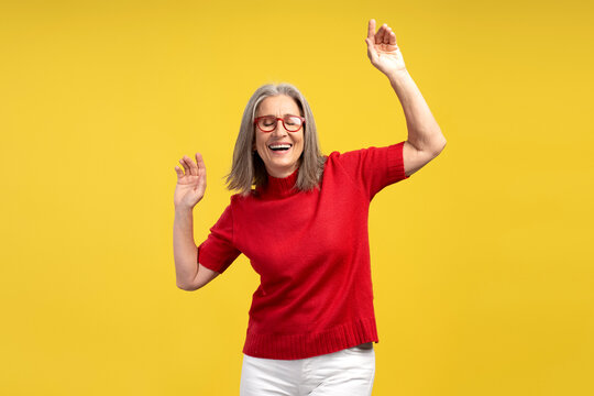 Happy, positive senior woman wearing stylish eyeglasses and red sweater dancing with closed eyes
