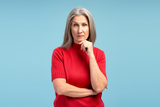Serious, pensive mature, gray haired woman wearing red sweater thinking, looking at camera - Powered by Adobe