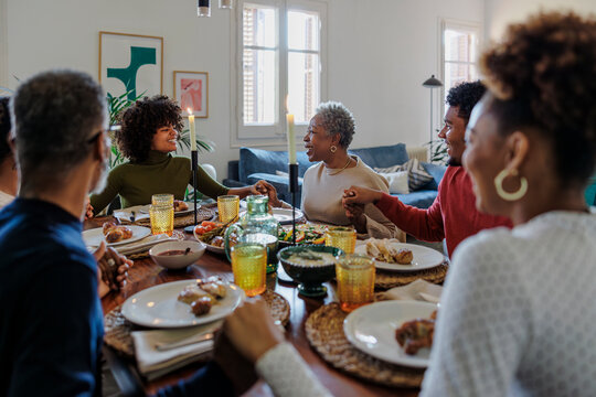 Family holding hands and saying grace before festive meal - Powered by Adobe