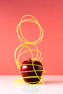 Sculpture like still life of an apple inside a neon tangled cable 