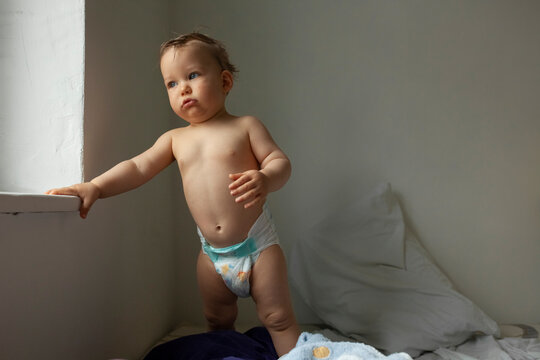 Portrait of a child in diapers stands by the window