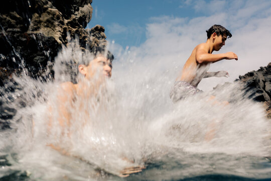 Cousins have fun splashing water during a dive into a natural pool