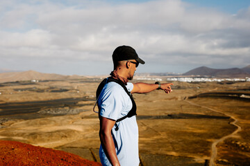 Sporty man gestures towards the horizon from the summit of a viewpoint