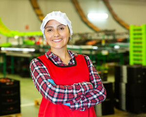 Portrait of positive female worker in uniform with arms crossed standing in fruit warehouse