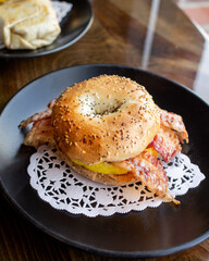 Everything bagel breakfast sandwich served with egg and bacon on black plate 