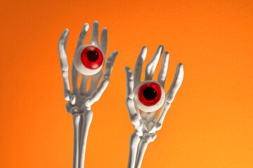Skeletal hands holding red eyeballs against a bright orange backdrop.