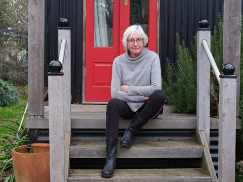 Elderly trans woman sitting on stairs of a cozy cottage