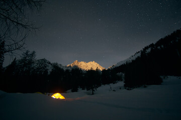 Bright tent glows under starry night sky in snowy mountain landscape