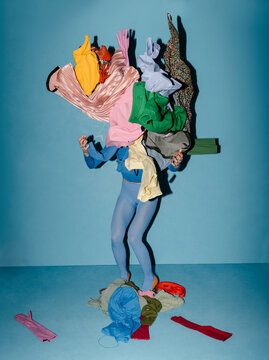 Person Overwhelmed by Colorful Clothes Against Blue Background