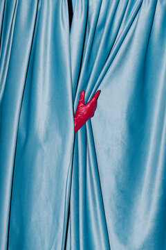 Red Gloved Hand Peeking Through Blue Curtains