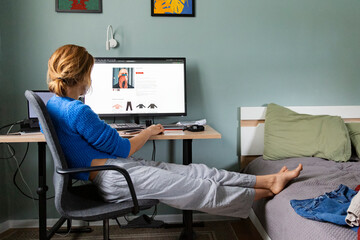 Woman browsing online fashion store with feet propped on bed

