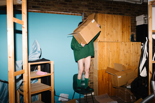 Person Balancing on Chair Holding Cardboard Box in Storage Room