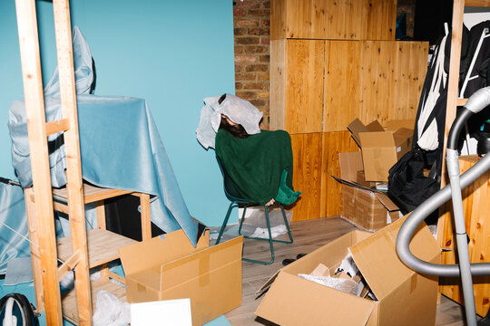 Cluttered Room with Person Under Blanket Surrounded by Boxes
