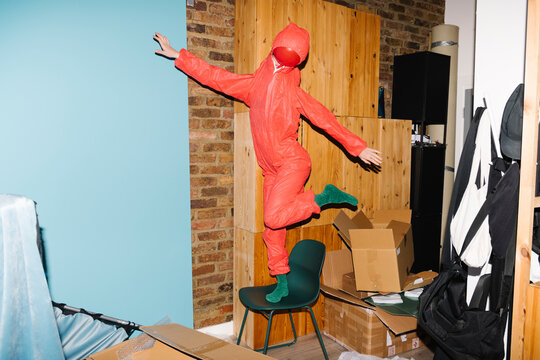 Person in Red Jumpsuit Balancing in a Messy Room