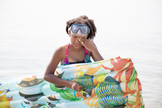 Child with floatie rubs water out of her eye as she exits a lake
