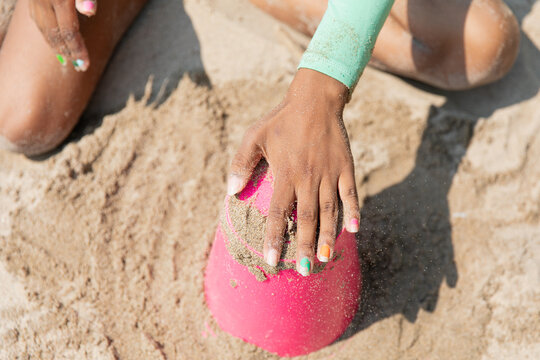 Closeup of a teen's hand as she makes a sandcastle with a red bucket

