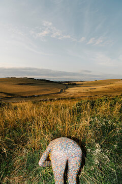 Person in Floral Suit Bending Over in Rural Field Landscape