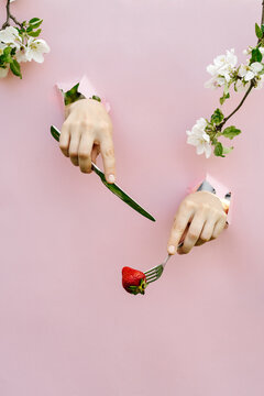 Hands emerging from pink poster with knife and strawberry on fork