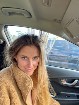 Woman with static hair sitting in car with slight smile.