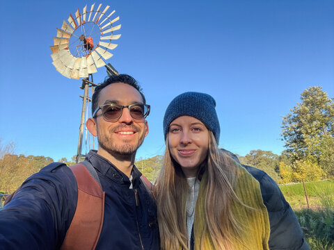 Couple poses with a windmill in the background, outdoors
