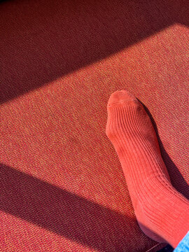 Single red sock on textured red surface with shadows