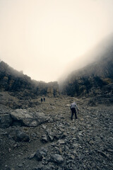 Hikers navigate rocky terrain under foggy conditions in a mountainous landscape