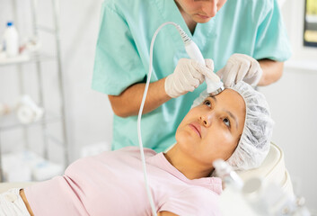Naklejka premium Doctor utilizes ultrasonic import attachment to enhance effectiveness of cosmetic treatment.