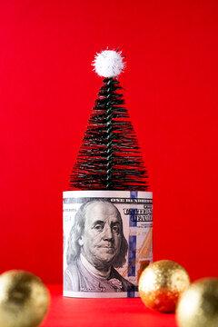 Christmas tree wrapped in one hundred dollar bill on red backgro