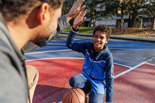 Son giving high five to father at basketball court