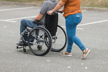 Personal assistant helping a man with disability to push a wheelchair outdoors. Help service concept.