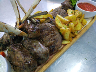 Veal rack with potato wedges and tomato sauce. delicious, hearty dish served on a wooden board. an appetizing dinner for the whole family. meat and vegetables