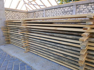 Stacked lumber on the street. Stacked wood for construction and repair work. Wooden planks close-up. Wooden beams for use in construction. Lots of planks in a warehouse