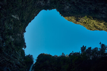 Clear blue sky framed by lush green cliffs in a remote valley during midday light