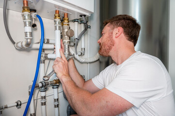 Installer carries out maintenance on a heat pump. Dressed in a white shirt, caucasian male with wrench in hand.