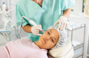 Young male cosmetologist performs facial cleansing procedure for young woman client