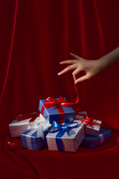 Hand Reaching for Ribbon on Stack of Festive Gift Boxes