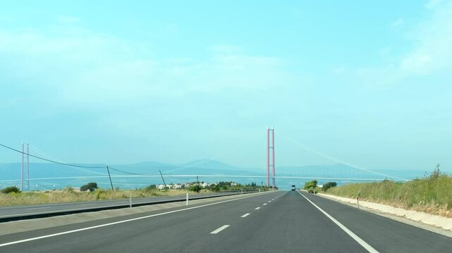 Car approaching the majestic bridge. Approaching the osman gazi bridge, the fourth longest suspension bridge globally, showcases a sunny day with clear blue skies and a scenic coastal landscape