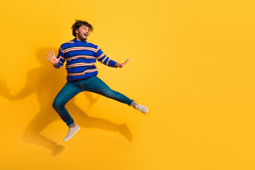 Full size photo of pretty young male jump have fun look empty space wear trendy blue striped outfit isolated on yellow color background