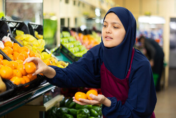 Woman vendor in hijab and apron takes ripe large mandarin from window.Concept of proper nutrition,healthy lifestyle