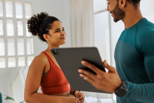 Personal trainer showing digital tablet to smiling client in gym