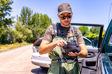 Young man preparing fishing gear by car